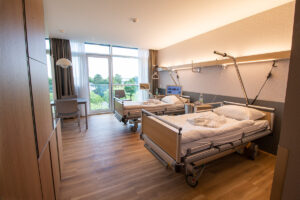 Patientenzimmer mit zwei Patientenbetten, Sitzecke mit Tisch und zwei Stühlen.